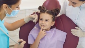 Child smiling in a dental chair with the dentist and assistant at a dental visit